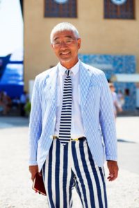 Man in striped suit outdoors, smiling.
