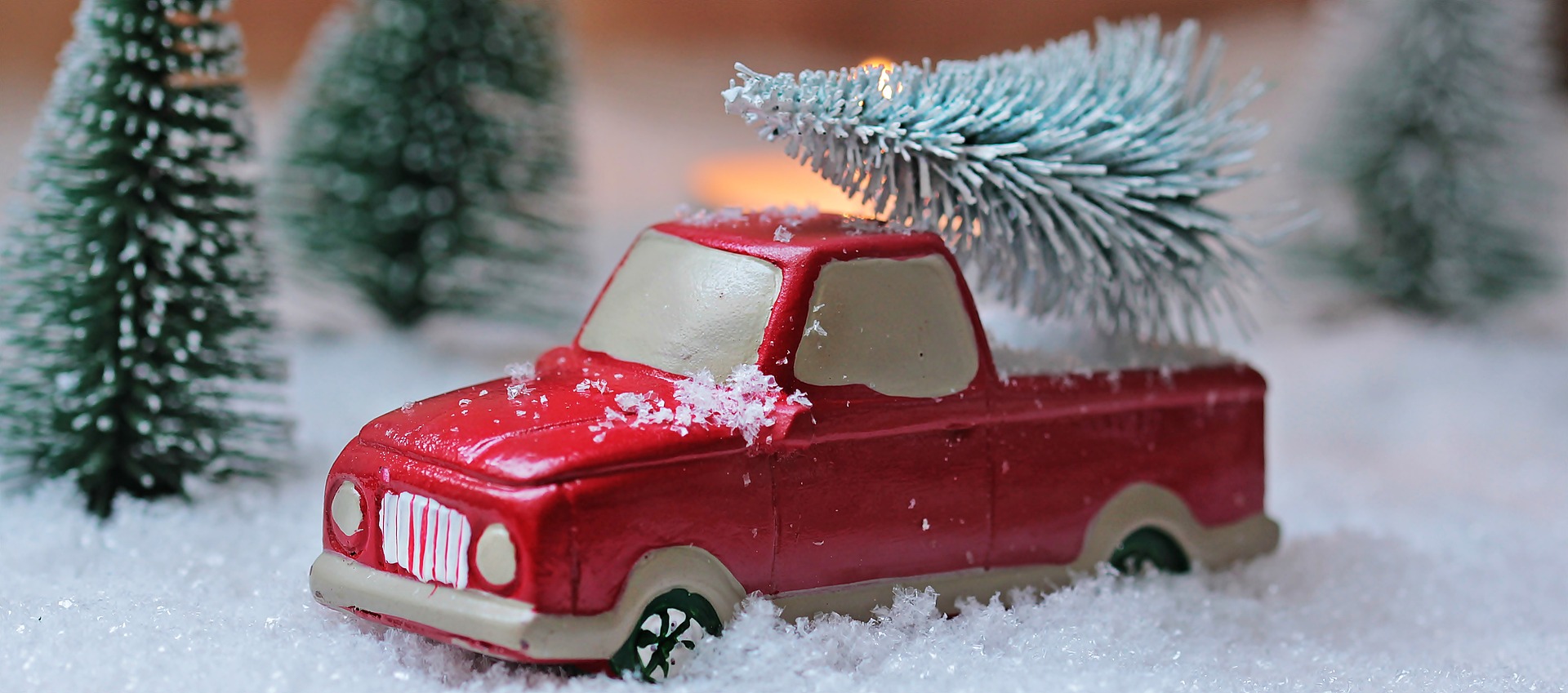 Red toy truck with Christmas tree in snow.